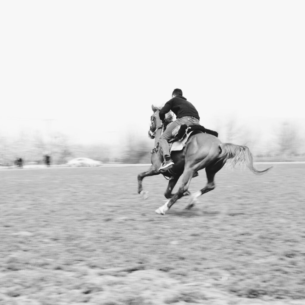 A black and white photo capturing a man racing on horseback through a countryside setting.